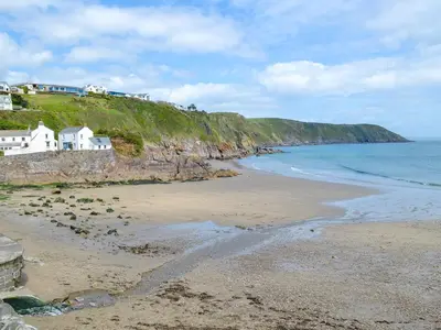 a beach with houses on a hill next to the ocean at Sea Haven - Tho in Gorran Haven