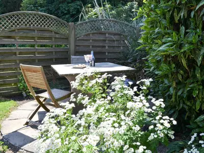 a table and bench in a garden with flowers at The Old Wash House in Pentewan