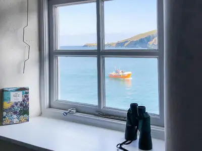 a window with a view of a boat in the water at Puffin Burrow in Portmellon