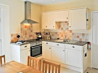 a kitchen with white cabinets and a table and a stove at The Gables in Gorran Haven