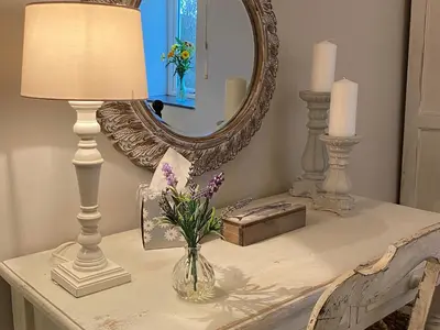 a table with a lamp and a mirror and flowers at Swallows Barn in Crowan