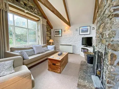 a living room with a couch and a tv and a stone wall at The Long Barn in Crowan