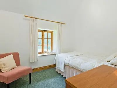 a bedroom with a bed and a chair and a window at Thatch Cottage in Saint Hilary