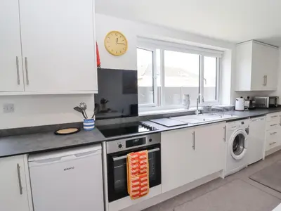 a kitchen with white cabinets and a clock on the wall at Sea Holly in St Ives