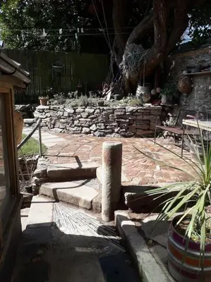 a garden with a stone wall and a potted plant at Bright cosy house, garden, central to town & beach in Falmouth