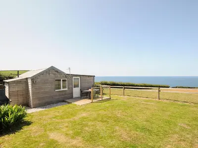 a small house in a yard with the ocean in the background at Lundy View Chalet in Bude