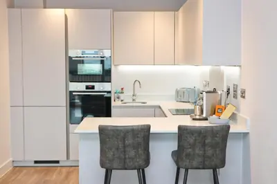 a kitchen with white cabinets and two bar stools at Sea view apartment, first floor in St Merryn