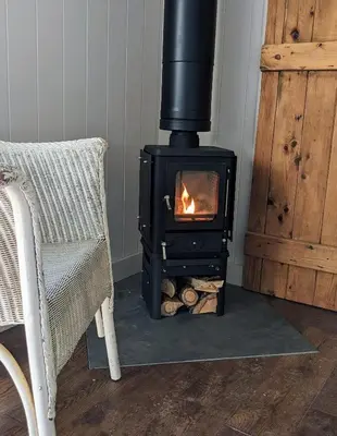 a stove with a fire in a room with a chair at The Applehay in Constantine