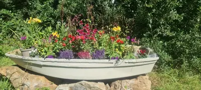 a white boat filled with flowers on top of rocks at Gillan Creek Retreat in Helston