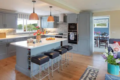 a kitchen with blue cabinets and a large island with bar stools at High Meadows in Saint Mawes
