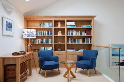 a home office with two blue chairs and a desk and book shelves at High Meadows in Saint Mawes