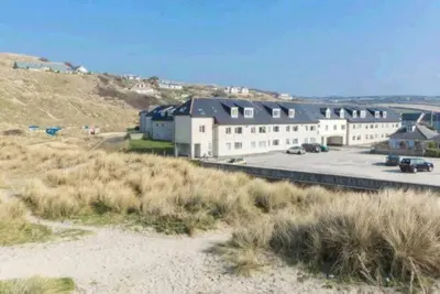a building on the side of a hill next to a beach at Direct Beach Access! Top Floor Apartment Perranporth in Perranporth