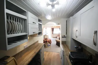 a kitchen with white cabinets and a living room at Briar Cottage in Looe