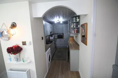 a kitchen with white cabinets and an archway at Briar Cottage in Looe