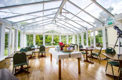 a conservatory with tables and chairs and windows at Polraen Country House Hotel in Looe