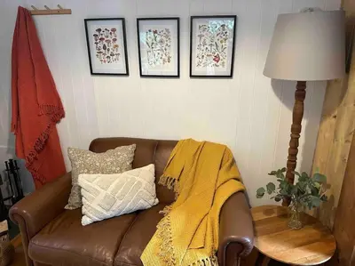 a living room with a brown couch with a yellow blanket at Cornwall Woodland Shepherd's Hut with Hot Tub - Deirdres Hut in Bodmin