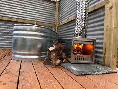 a fireplace and a teddy bear sitting next to a barrel at Cornwall Woodland Shepherd's Hut with Hot Tub - Deirdres Hut in Bodmin