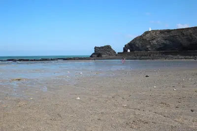 a beach with a rocky shoreline with a lighthouse in the background at Apple Tree Bungalow in Redruth