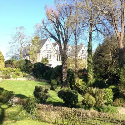 a white house with trees and bushes in a yard at Riverside Apartment in Uny Lelant