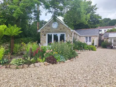 a stone house with a clock on the front of it at Tree Fern Barn in St Austell