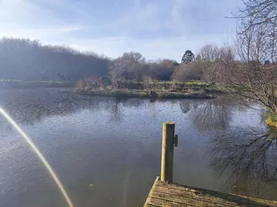 a body of water with a dock in the middle at Tree Fern Barn in St Austell