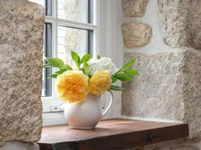 a white vase with yellow and white flowers on a window sill at The Hayloft in Helston