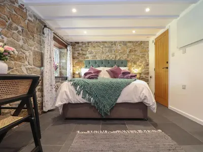 a stone walled bedroom with a bed and a stone wall at The Hayloft in Helston