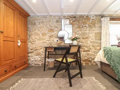 a bedroom with a table and a chair in front of a stone wall at The Hayloft in Helston