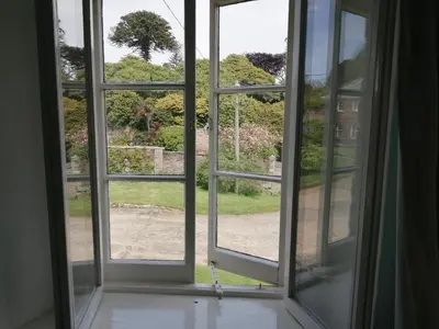 an open window with a view of a garden at The Old Stables of heritage Tregrehan Garden Cottages on South Coast in St Austell
