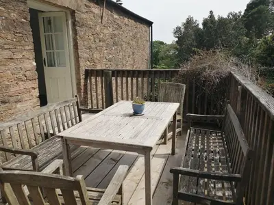 a wooden table and two benches on a deck at The Old Stables of heritage Tregrehan Garden Cottages on South Coast in St Austell