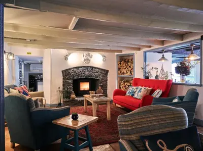 a living room with a red couch and a fireplace at Lugger Hotel ‘A Bespoke Hotel’ in Portloe