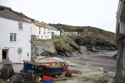 a boat sitting on the beach next to a house at Lugger Hotel ‘A Bespoke Hotel’ in Portloe