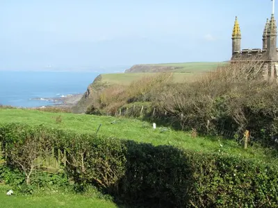 a grassy hill with a castle and the ocean at Church Cottage in Bude