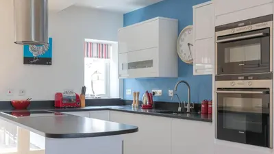 a kitchen with white cabinets and blue walls at Castle House - Penthouse in Polruan