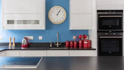 a kitchen with a clock on a blue wall at Castle House - Penthouse in Polruan