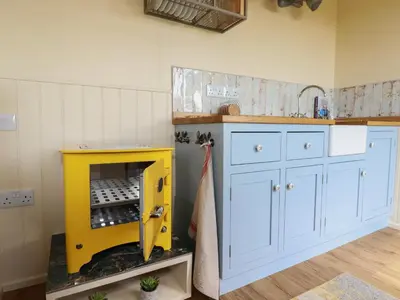 a kitchen with a yellow cabinet and a shelf at Dot May in Wadebridge