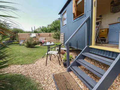 a small garden with a table and a blue house at Dot May in Wadebridge