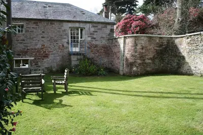 a bench sitting in a yard next to a brick wall at Gamekeeper's Cottage within historic Tregrehan Garden in Par