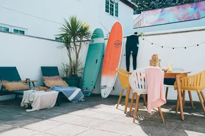 a table and chairs and surfboards leaned against a wall at Apartment 3 Fistral Beach in Newquay