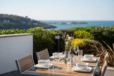 a wooden table with chairs and a table with wine glasses at Barepta Cove, Stunning Carbis bay apartment in Carbis Bay