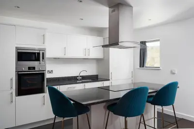 a kitchen with white cabinets and a table with blue chairs at Barepta Cove, Stunning Carbis bay apartment in Carbis Bay