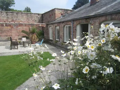 a garden with white flowers in front of a building at The Coach House within heritage Tregrehan Garden on Cornwall's South Coast in Carlyon Bay