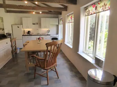 a kitchen with a wooden table and chairs and windows at The Coach House within heritage Tregrehan Garden on Cornwall's South Coast in Carlyon Bay