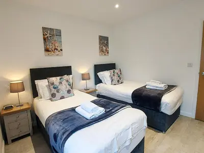 two beds in a room with two lamps and towels at Meadow View Apartments in Newquay