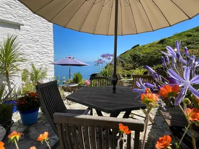 a wooden table with an umbrella and some flowers at Just Opened. Romantic Clifftop Retreat in Portloe