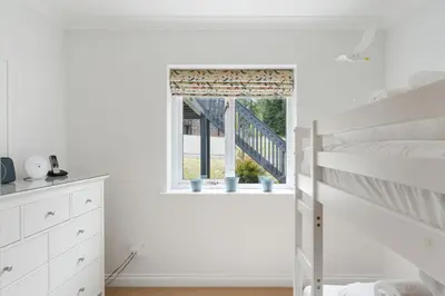 a white bedroom with a bunk bed and a window at The Hawthorns in Polzeath