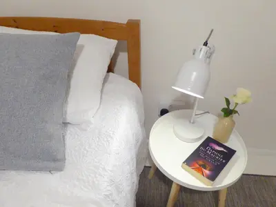 a bed with a table with a book and a lamp at Churchtown Cottage in Cubert