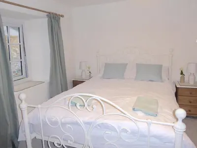 a bedroom with a white bed with blue pillows at Churchtown Cottage in Cubert