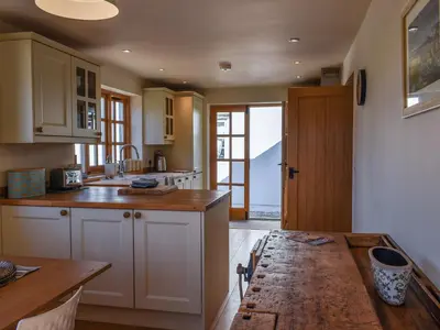 a kitchen with white cabinets and a wooden table at The Potting Shed in Par