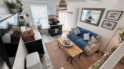 a living room with a blue couch and a table at SMUGGLERS HIDE or SMUGGLERS CABIN - EITHER a 2 Bedroom FISHERMANS COTTAGE with Childs Bunk and HARBOUR VIEWS - OR a ground floor private small CABIN ROOM - 10 Metres To Sea Front - Book Both for a 3 Bed House - 2023 GLOBAL REFURBISHMENT AWARD WINNER in St Ives